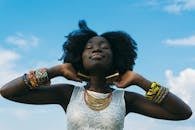 Portrait of a joyful African woman with afro hair, wearing colorful bracelets and gold earrings, enjoying the sunny day.